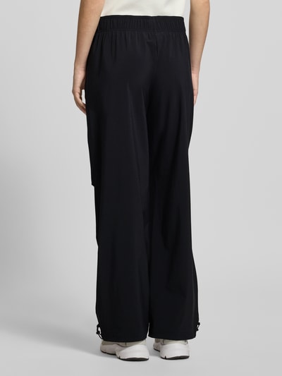 Frauenmodel trägt Wide Fit Stoffhose mit Logo-Print von adidas Sportswear in Schwarz, elastischer Bund, glatte Textur, Ganzkörperansicht Rückansicht.