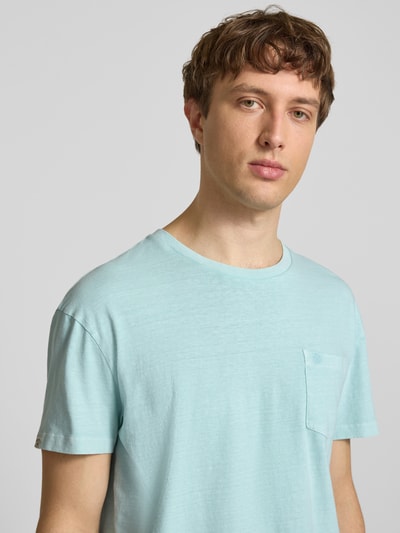 Männermodel trägt T-Shirt aus Baumwoll-Leinen-Mix mit Brusttasche von Superdry in Hellblau, Regular Fit, Rundhalsausschnitt, Nahaufnahme Oberkörper.