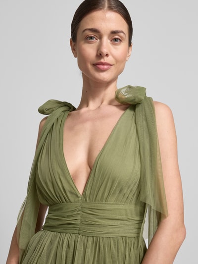Frauenmodel trägt Knielanges Kleid mit Rüschenbesatz von LACE & BEADS in Grün aus Mesh, taillierte Passform, V-Ausschnitt, Zierschleifen, Nahaufnahme Oberkörper.