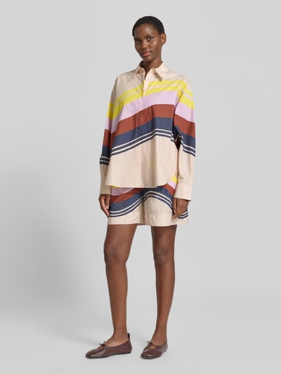 Frauenmodel trägt Boxy Fit Langarmbluse aus reiner Baumwolle Modell 'JOPPY' von Essentiel Antwerp, bunt gestreift, Ganzkörperansicht von vorne.