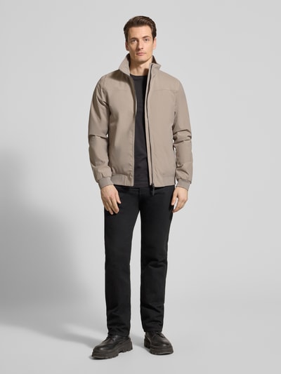 Männermodel trägt Regular Fit Jacke mit Stehkragen Modell 'Alvin' von Didriksons in Beige, Reißverschluss, elastische Abschlüsse, Eingrifftaschen, Ganzkörperansicht von vorne. Rückenlänge 69 cm, Schulterbreite 44 cm, Brustweite 54 cm, Ärmellänge 70 cm, Größe M.