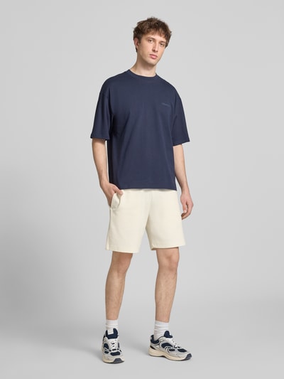 Männermodel trägt Shorts mit elastischem Bund und Label-Stitching von CHAMPION im Regular Fit, helle Farbe, Baumwoll-Mix, Ganzkörperansicht von vorne.