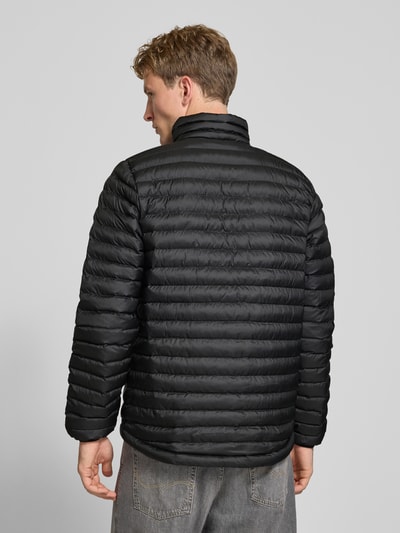 Männermodel trägt Steppjacke mit Label-Print von Helly Hansen in Schwarz, horizontale Steppung, Ganzkörperansicht Rückansicht. Rückenlänge 72 cm, Schulterbreite 42 cm, Brustweite 54 cm, Ärmellänge 72 cm, gerade Passform, Stehkragen, elastische Ärmelabschlüsse.