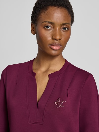 Vrouwenmodel draagt Regular Fit Minikleid uit viscosemix Model 'Abito' van Liu Jo met siersteentjes, serafinohals, detailopname bovenlichaam. Context: Dames mini-jurk van Liu Jo Sport, elastische viscosemix, regular fit, Model 'Abito', met siersteentjes, met lange mouwen, serafinohals, ruglengte maat S: 88 cm, borstwijdte maat S: 50 cm, mouwlengte maat S: 61 cm.
