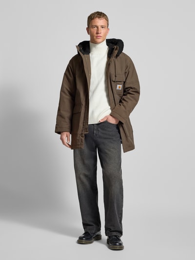 Mannenmodel draagt Regular fit Parka met Logopatch model 'Siberia' van Carhartt Work In Progress in bruin met klepzakken, borstzak, capuchon met tunnelkoord, ritssluiting met afdekstrip, context heren parka, ruglengte 88 cm, schouderbreedte 47 cm, borstwijdte 64 cm, mouwlengte 65 cm, geheel lichaamsaanzicht vooraan