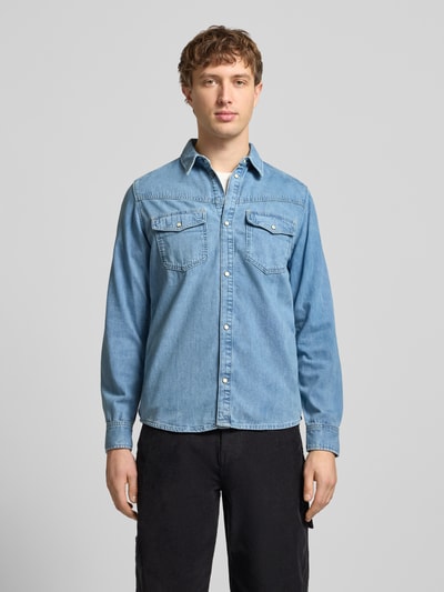 Männermodel trägt Regular Fit Jeanshemd aus reiner Baumwolle Modell 'BROOKS' von Pepe Jeans in Denim-Optik mit Kentkragen, Brusttaschen, Druckknöpfe, Rückenpasse, Langarm mit Manschette und leicht abgerundetem Rumpfabschluss. Ganzkörperansicht von vorne.