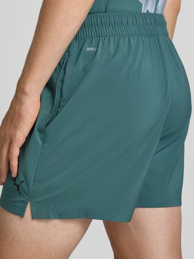 Männermodel trägt Regular Fit Sportshorts mit Logo-Print Modell 'TAD ESSENTIALS' von PUMA in dunklem Türkis, Detailaufnahme Rückansicht, Kontext: Herren Sportshorts von PUMA Performance.