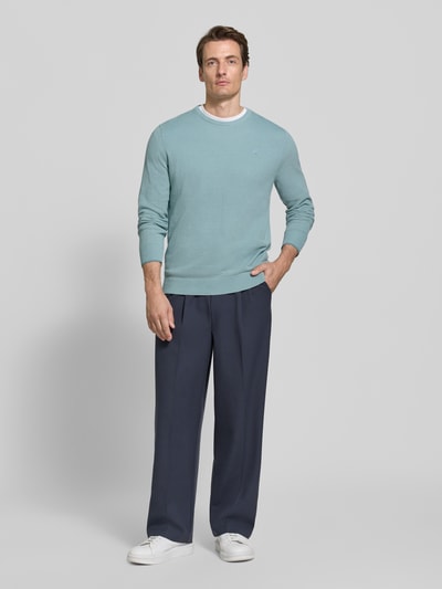 Männermodel trägt Regular Fit Strickpullover aus reiner Baumwolle mit Label-Detail von LERROS in Hellblau, kombiniert mit dunkelblauer Hose, elastische Abschlüsse, Ganzkörperansicht von vorne.