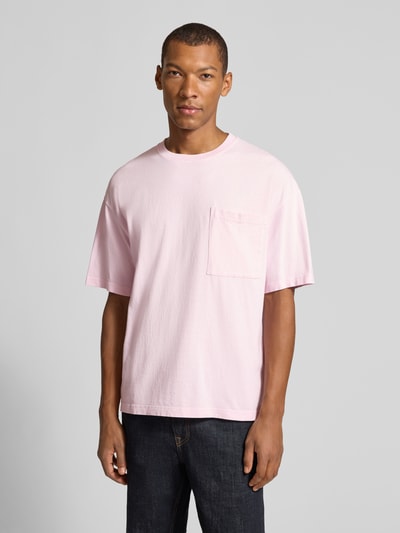 Männermodel trägt T-Shirt aus reiner Baumwolle mit Brusttasche Modell 'AFOMA' von American Vintage in Rosa, Relaxed Fit, Ganzkörperansicht von vorne.