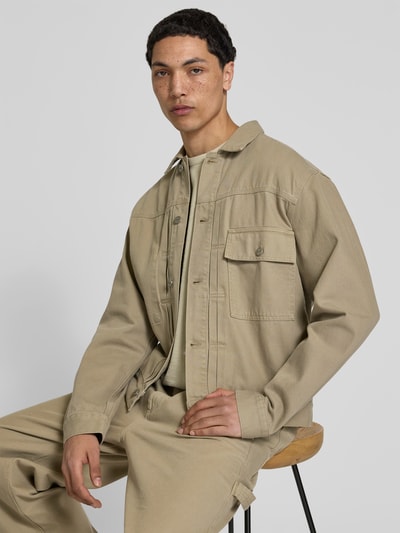 Männermodel trägt Jeansjacke aus Reiner Baumwolle von Forét, Regular-Fit, Durchgehende Knopfleiste, Brusttasche, Umlegekragen, Nahaufnahme Oberkörper.