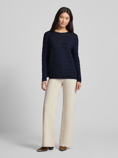 Frauenmodel trägt Regular Fit Pullover aus reiner Baumwolle in Strick-Optik von Christian Berg Woman, dunkelblau, semitransparent, beige Hose, Ganzkörperansicht von vorne.