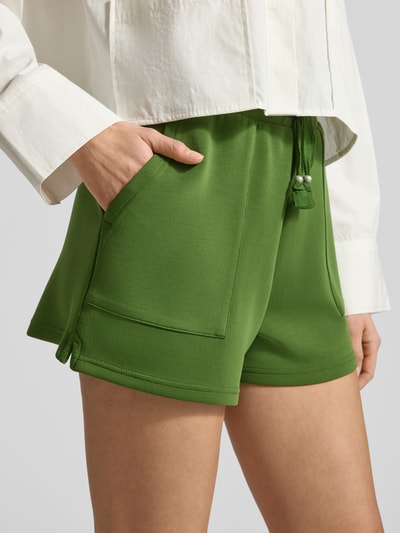 Frauenmodel trägt Sweatshorts mit Seitentaschen von Scotch & Soda in Grün, elastischer Bund, seitliche Taschen, Nahaufnahme Oberkörper.