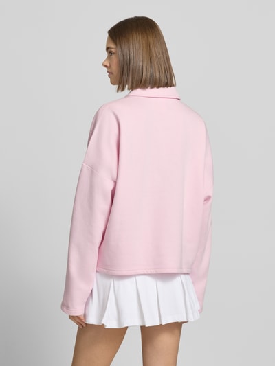 Frauenmodel trägt Sweatshirt mit Label-Print von adidas Sportswear in Rosa, lockerer Schnitt, Hemdblusenkragen, Rückansicht Ganzkörperansicht.