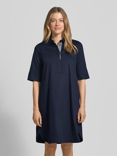 Frauenmodel trägt knielanges Hemdblusenkleid mit Eingrifftaschen von Christian Berg Woman aus reiner Baumwolle in Dunkelblau, gerader Schnitt, verdeckte Knopfleiste, Halbarm, Ganzkörperansicht von vorne.