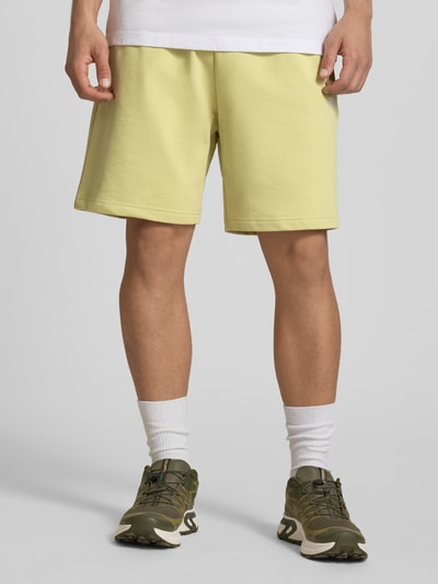 Męski model nosi Sweatshorts mit Logo-Stitching od The North Face, kolor jasnożółty, bawełna, krój relaxed fit, elastyczny pas z troczkiem, szerokość w rozmiarze M: 40 cm, długość nogawki wewnętrznej w rozmiarze M: 18 cm, logo z przeszyciem, widok całej sylwetki z przodu.
