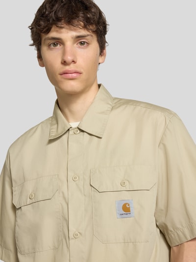 Männermodel trägt Relaxed Fit Freizeithemd mit Kentkragen und Label-Detail von Carhartt Work In Progress, Material-Mix, Nahaufnahme Oberkörper. Rückenlänge 75 cm, Schulterbreite 51 cm, Ärmellänge 28 cm, Cremefarbe, strukturierte Oberfläche, zwei Brusttaschen.