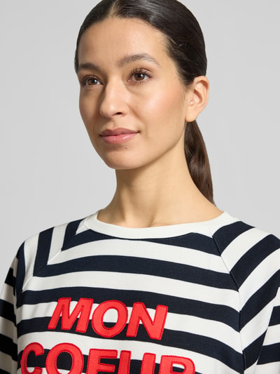 Frauenmodel trägt Sweatshirt mit Rundhalsausschnitt und 3/4-Arm von More & More, gestreiftes Design, Statement-Print, Nahaufnahme Oberkörper.