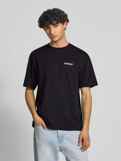 Männermodel trägt schwarzes Relaxed Fit T-Shirt aus reiner Baumwolle Modell 'FRED DU MARTIN' von Only & Sons, Motiv-Print, Ganzkörperansicht von vorne.