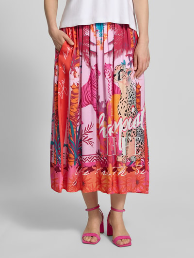 Frauenmodel trägt Midirock aus reiner Viskose mit Allover-Motiv-Print von miss goodlife in Pink mit elastischem Bund, A-Linie, Nahaufnahme Unterkörper. Damen Midirock, Bundweite 35 cm, Gesamtlänge 82 cm, Größe S.