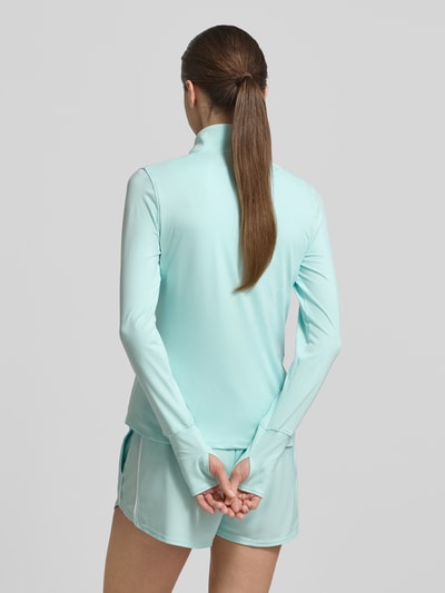 Frauenmodel trägt Longsleeve mit Stehkragen und Reißverschluss von Under Armour in hellem Türkis, Material mit Stretch, Rückenlänge 59 cm, Ganzkörperansicht Rückansicht.