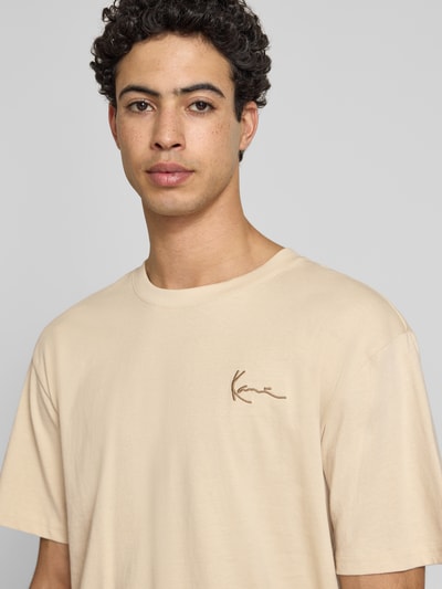 Männermodel trägt Relaxed Fit T-Shirt mit Logo-Stitching von KARL KANI aus Reine Baumwolle in Beige, Rundhalsausschnitt, Nahaufnahme Oberkörper.
