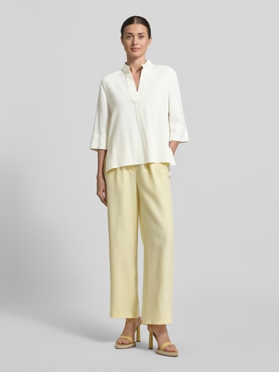 Frauenmodel trägt Regular Fit Bluse aus Viskose-Elasthan-Mix mit 3/4-Arm von Luisa Cerano in Creme, kombiniert mit hellgelber Hose, glatte Textur, Ganzkörperansicht von vorne. Rückenlänge bei Größe 36: 66 cm, Ärmellänge 53 cm, Stehkragen.