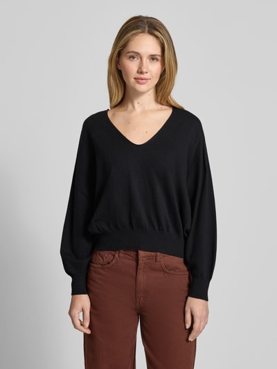 Kobiece modelka nosi czarny Sweter z dzianiny z mieszanki bawełny i kaszmiru Model 'RISORY' od Drykorn, krój relaxed fit, dekolt w serek, długość tyłu w rozmiarze S: 53 cm, długość rękawów w rozmiarze S: 48 cm, widok całej sylwetki z przodu