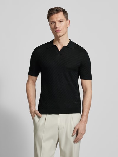 Männermodel trägt schwarzes Slim Fit Poloshirt mit Lyocell-Anteil von Emporio Armani, Strick-Optik, Kurzarm, Ganzkörperansicht von vorne.