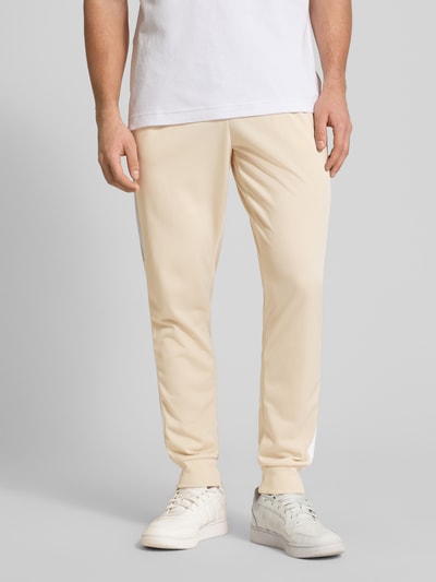 Männermodel trägt Regular Fit Sweat-Anzug mit Kontraststreifen von adidas Sportswear, unifarben, Beinabschluss gerippt, Nahaufnahme Unterkörper.