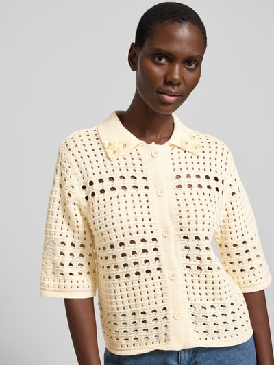 Frauenmodel trägt Regular Fit Bluse in Strick-Optik mit floralem Ziersteinbesatz von Liu Jo White, Reine Baumwolle, Lochmuster, Halbarm, Umlegekragen, durchgängige Knopfleiste, cremefarbene Struktur, Nahaufnahme Oberkörper.
