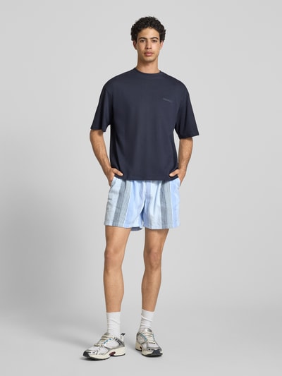 Męski model nosi Relaxed Fit Shorts aus reiner Baumwolle od Tommy Jeans, efekt: wzór na całej powierzchni, naszywka z logo, elastyczny ściągacz z tunelem, wpuszczane kieszenie, wykończenie materiału: dobby, bawełna, widok całej sylwetki z przodu.
