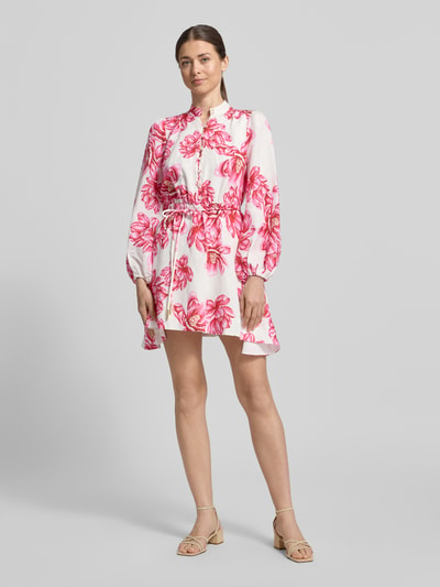 Kobiece modelka nosi sukienkę mini z mieszanki lnu i dodatkiem wiskozy model 'Annalise' od Forever New, kwiatowy nadruk na całej powierzchni, taliowany krój, długie rękawy, stójka, listwa guzikowa, zakończenia rękawów wykończone lamówką, długość tyłu w rozmiarze 36: 82 cm, szerokość w rozmiarze 36: 38 cm, długość rękawa w rozmiarze 36: 59 cm, jasne kolory, różowe wzory, prosty materiał, gładka faktura, widok całej sylwetki od przodu.