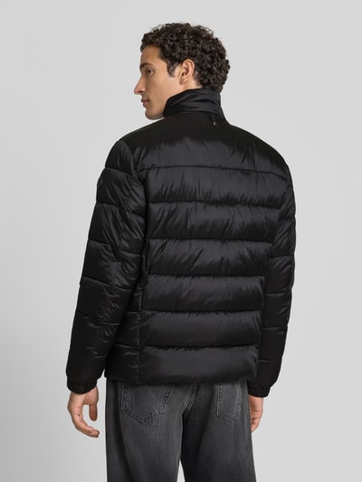 Männermodel trägt Regular Fit Steppjacke mit Stehkragen von JOOP! COLLECTION in Schwarz, dezente Steppstruktur, Ganzkörperansicht Rückansicht.