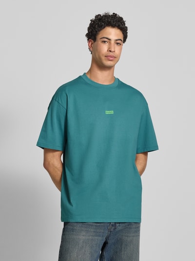 Männermodel trägt Oversized T-Shirt aus reiner Baumwolle Modell 'NALONO' von Hugo Blue in Unifarbe mit Label Print, Rundhals, kurzarm, Webware, Ganzkörperansicht von vorne.