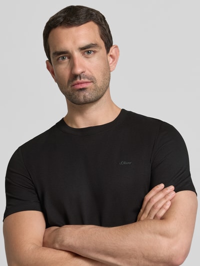 Męski model nosi Regular Fit T-Shirt aus reiner Baumwolle von s.Oliver RED LABEL, czarny kolor, gładka tekstura, zbliżenie na górną część ciała.
