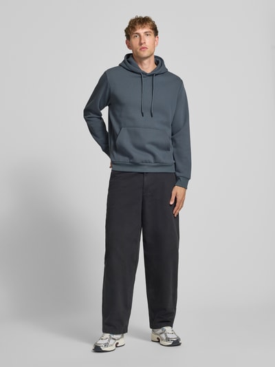 Männermodel trägt Hoodie mit Känguru-Tasche Modell 'BRADLEY' von JACK & JONES in Blau, lockerer Schnitt, Ganzkörperansicht von vorne.