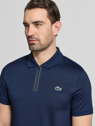 Männermodel trägt Slim Fit Poloshirt aus schnelltrocknendem Material von Lacoste, Optik: Unifarben, Logo-Patch, Nahaufnahme Oberkörper.