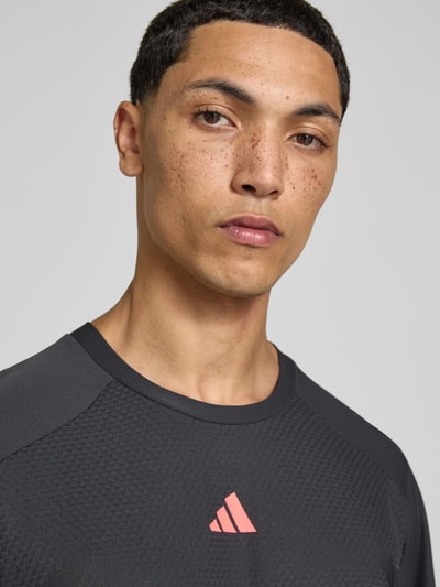 Männermodel trägt Regular Fit Sport-T-Shirt mit Logo-Print Modell '3D WC TEE' von adidas, schwarz mit rotem Logo, adidas Training, Nahaufnahme Oberkörper.