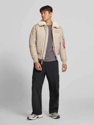 Männermodel trägt Bomberjacke mit Label-Patch und Kentkragen von Alpha Industries in Beige, Teddyfell-Kragen, Ganzkörperansicht von vorne. Regular Fit, Reißverschluss, Reißverschlusstasche am Ärmel mit Label-Patch, Eingrifftaschen mit Druckknopfverschluss, gerippte Abschlüsse, Rückenlänge 65 cm, Schulterbreite 45 cm, Brustweite 56 cm, Ärmellänge 65 cm.