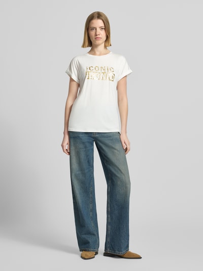 Frauenmodel trägt T-Shirt mit Rundhalsausschnitt und Print Modell 'MARICA' von Soyaconcept, weiß mit Goldprint, Relaxed Fit, Lyocell-Elasthan-Mix, Ärmel mit Aufschlag, Ganzkörperansicht von vorne.