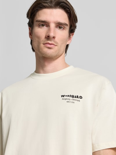 Mężczyzna model nosi T-Shirt mit Label-Print Modell 'Baine' von WOODBIRD z czystej bawełny, krój regular fit, jasny kolor, zbliżenie na górną część ciała.