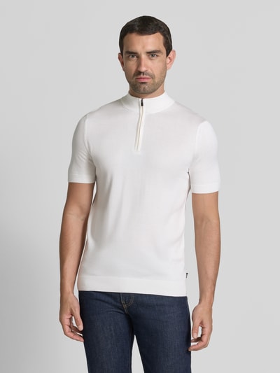 Męskmodel nosi Strickshirt aus Viskose-Mix mit Stehkragen Modell 'Vadin' von JOOP! COLLECTION, mieszanka wiskozy, dopasowany krój, prążkowana stójka, krótki zamek błyskawiczny, długość tyłu w rozmiarze M: 68 cm, długość rękawów w rozmiarze M: 24 cm, biała gładka dzianina, prosty fason, Ganzkörperansicht von vorne.