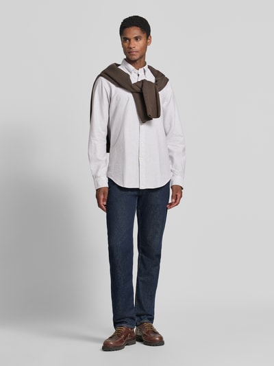 Męski model nosi Super Slim Fit Freizeithemd aus reiner Baumwolle od Polo Ralph Lauren, jasna koszula casualowa, ciemne jeansy, brązowy sweter na ramionach, Ganzkörperansicht von vorne.