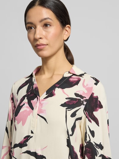 Modelka kobieca ma na sobie Blusenshirt mit V-Ausschnitt Modell 'BENE' od Soyaconcept z czystej wiskozy w kremowe tło z czarno-różowym wzorem, luźny krój, dekolt V, marszczenia, długość tyłu w rozmiarze S 66 cm, długość rękawa 63 cm, zbliżenie na górną część ciała.