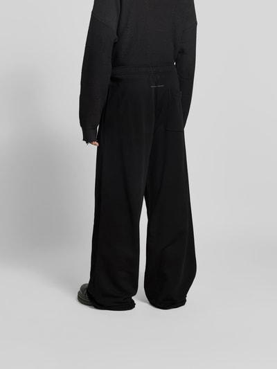 Männermodel trägt Wide Fit Stoffhose mit Gesäßtasche von MM6 Maison Margiela, schwarze Baumwolle, elastischer Bund, Ganzkörperansicht Rückansicht.
