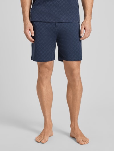 Männermodel trägt Shorts aus Baumwolle mit Logo-Muster von JOOP! Collection in Dunkelblau, Regular-Fit, Ganzkörperansicht von vorne.