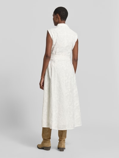 Frauenmodel trägt Maxikleid mit Bindegürtel Modell 'CATA' von Mango aus weißer Baumwolle mit Umlegekragen und Knopfleiste, Ganzkörperansicht Rückansicht.