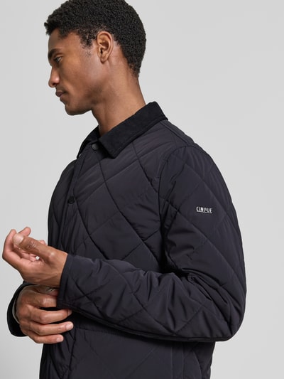 Männermodel trägt Regular Fit Jacke in Stepp-Optik Modell 'Rapid' von CINQUE, schwarze Farbe, seitliche Nahaufnahme Oberkörper. Elastischer Material-Mix, aufgesetzte Taschen, Umlegekragen, Knopfleiste.