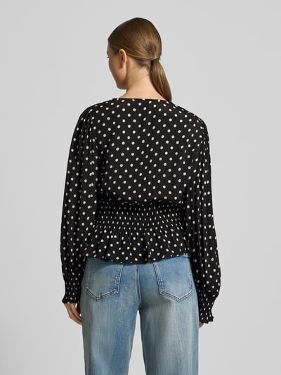 Frauenmodel trägt Bluse aus reiner Viskose in Wickel-Optik Modell 'Tamona' von Neo Noir, schwarz mit weißen Punkten, langärmelig, taillierte Passform, Rüschenbesatz, Ganzkörperansicht Rückansicht.