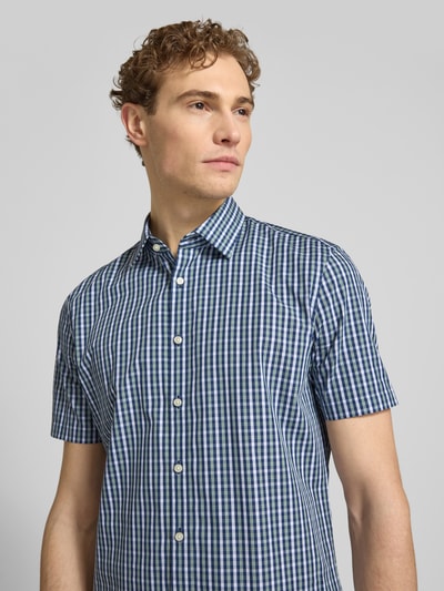 Męski model nosi Slim Fit Business-Hemd aus Baumwolle mit Kentkragen von Jake*s, krój slim fit, bawełna, listwa guzikowa, rękaw o dł. 1/2, długość tyłu w rozmiarze 39/40: 79 cm, szerokość w rozmiarze 39/40: 48 cm, długość rękawów w rozmiarze 39/40: 23 cm, wzór w kratę, odcienie niebieskiego i zielonego, tekstura gładka, widok na górną część ciała z przodu.